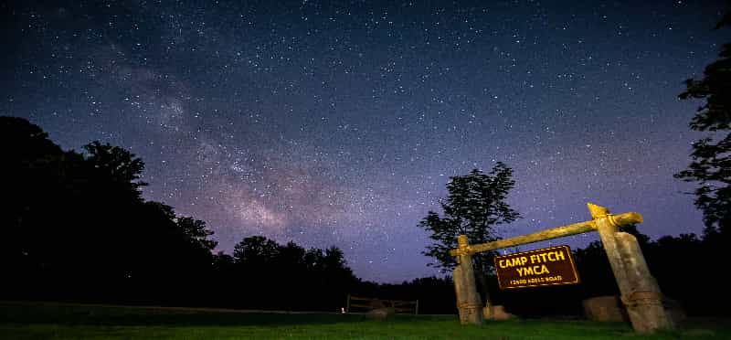 a sign in a field with trees and stars in the sky
