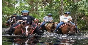 a group of people riding horses through a river