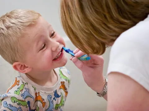 a person brushing a kid's teeth