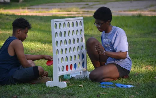 a couple of boys sitting on the grass next to a sign