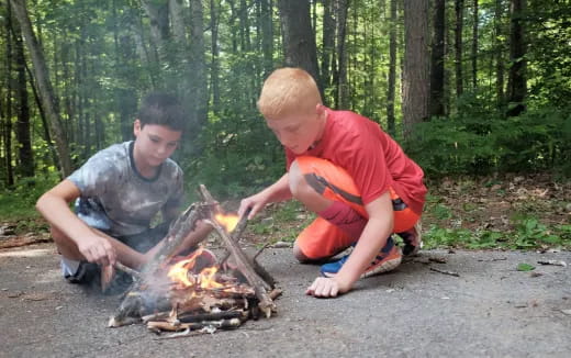 two boys sitting next to a fire