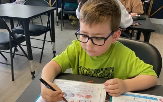 a boy sitting at a table writing on a piece of paper