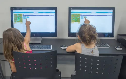 a couple of girls sitting at a desk with computers
