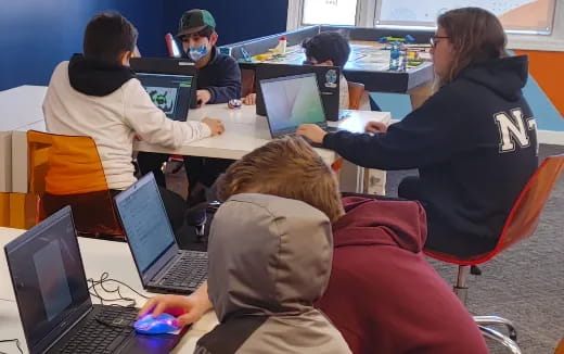 a group of people sitting at a table with laptops