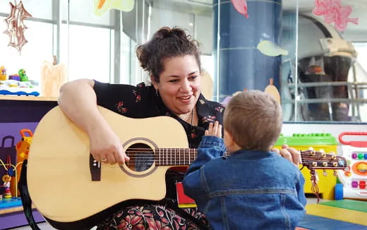 a person playing a guitar to a young boy