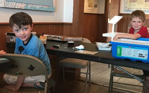 a couple of boys sitting at a table with laptops