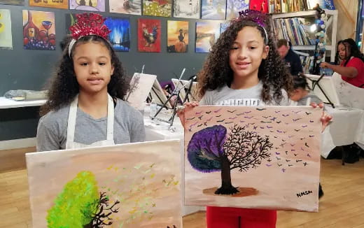 a couple of girls sitting at a table with art on it