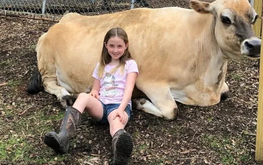 a girl kneeling next to a cow
