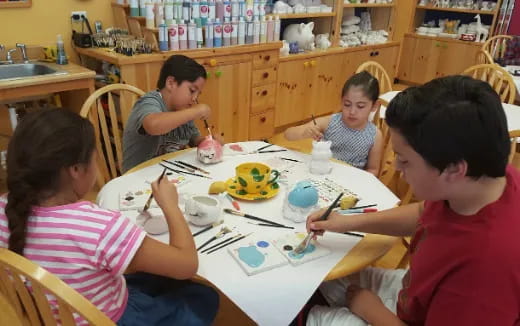 a group of people sitting around a table painting