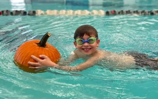 a boy in a pool with a pumpkin