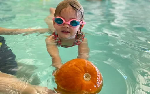 a child in a pool with a ball in her mouth