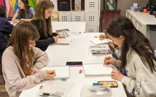 a group of girls sitting at a table writing on paper
