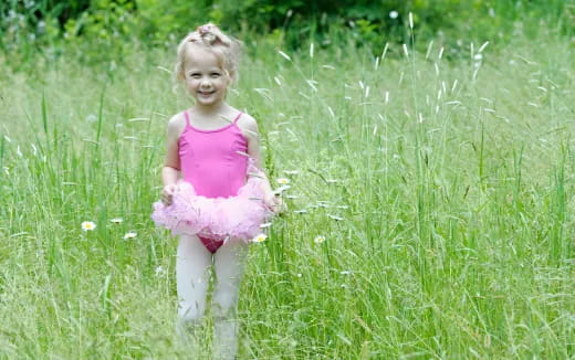 a girl in a pink dress standing in a grassy field