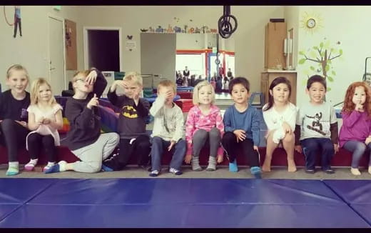 a group of children sitting on a blue mat in a room