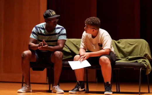 a couple of men sitting on a couch looking at a paper