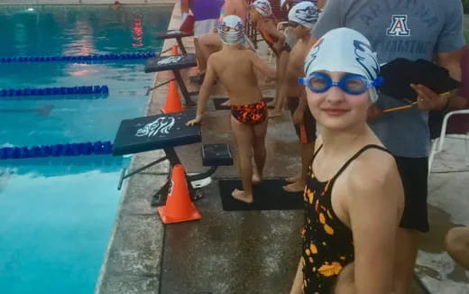 a boy in a swimsuit by a pool with other people