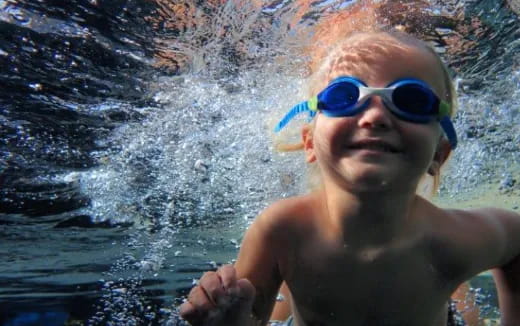 a boy wearing sunglasses and swimming in water
