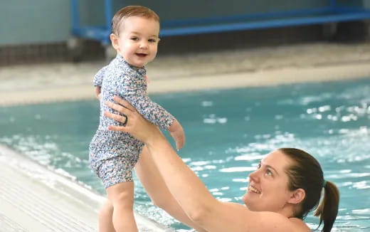 a woman holding a baby by a pool