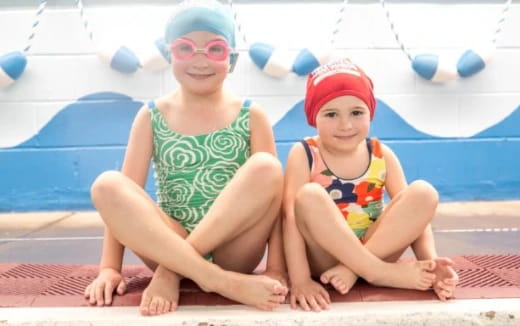 a couple of children sitting on a mat by a pool
