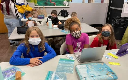 a group of children sitting at a table with a laptop