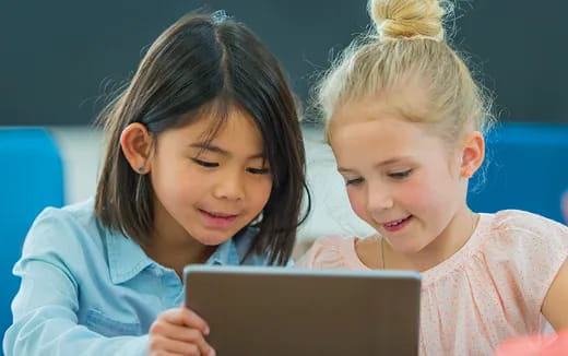 a couple of young girls looking at a tablet