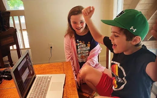 a boy and girl sitting at a table with a laptop