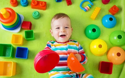 a baby lying on a green surface with colorful toys