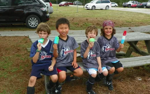 a group of kids sitting on a bench holding green cups