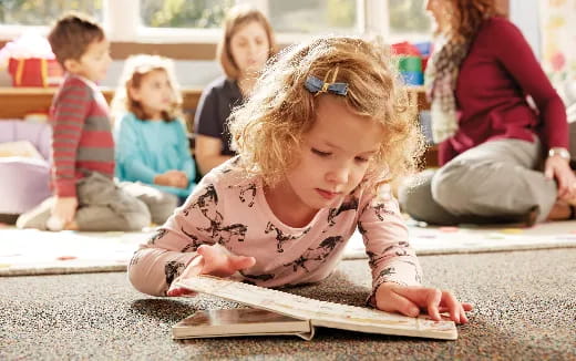 a young girl sitting on the floor reading a book