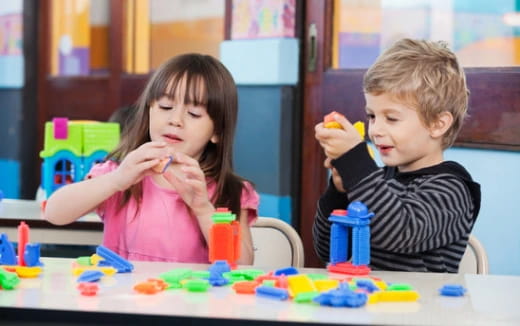 a boy and girl sitting at a table with toys