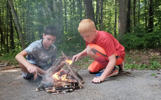 two boys sitting next to a fire