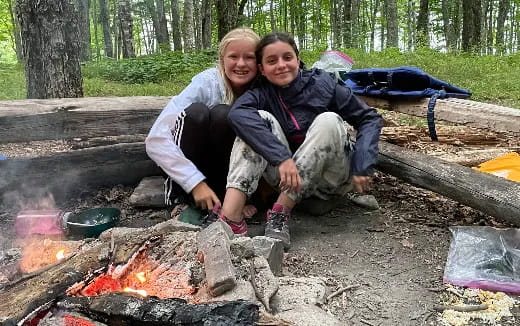 a man and woman sitting on a fire in the woods