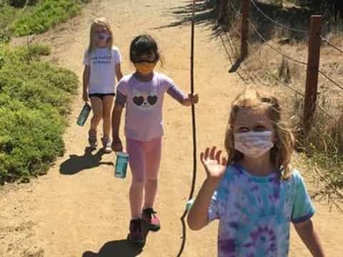 a group of children walking on a path with a rope and a fence