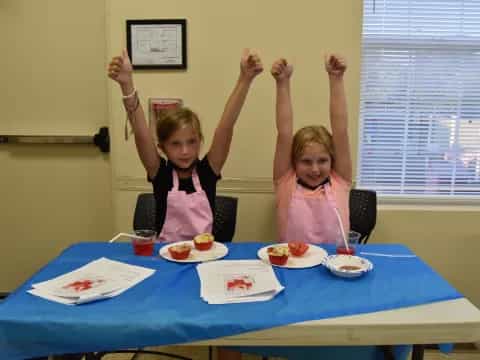 two girls sitting at a table with food on it
