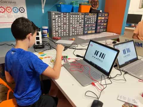 a boy sitting at a desk with a laptop and a computer