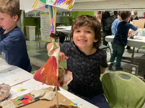 a boy sitting at a table with a kite and other people