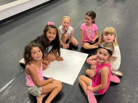 a group of girls sitting on the ground and holding a paper