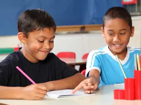 a couple of boys sitting at a table looking at a paper