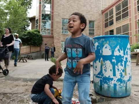 a boy standing next to a blue barrel