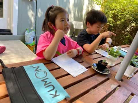a couple of kids sitting at a table with food and a spoon