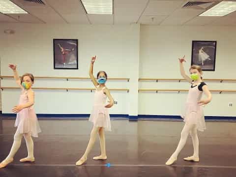 a group of girls in white outfits dancing in a room with pictures on the wall