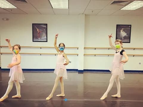 a group of girls in white outfits dancing in a room with pictures on the wall