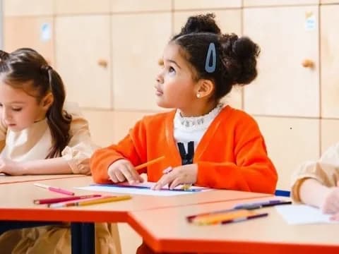 a few young girls sitting at a table writing on paper