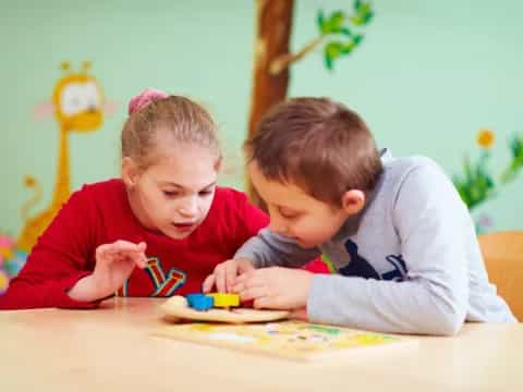 a couple of young children sitting at a table looking at a book