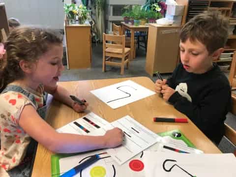 a couple of kids sitting at a table with papers and pens
