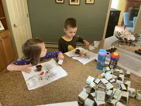 a couple of kids sitting at a table with a cake and some food