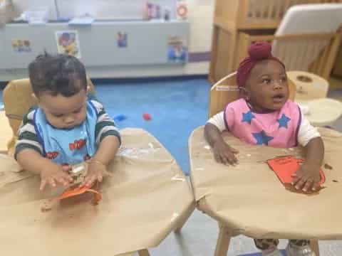 a couple of young girls sitting at a table with a carrot