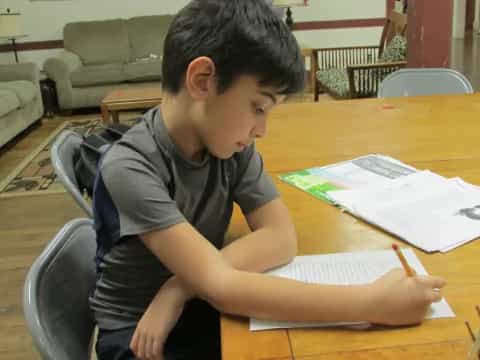 a boy sitting at a table writing on a piece of paper