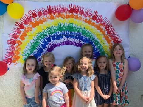 a group of girls posing for a picture with a rainbow umbrella
