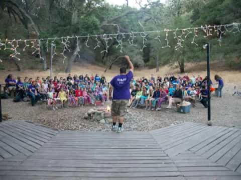a person standing on a deck with a group of people sitting on the ground